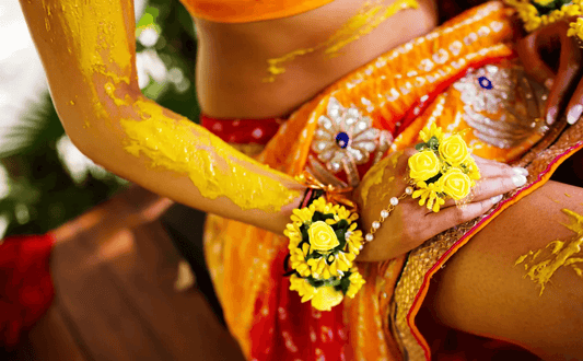 Woman adorned in traditional attire with turmeric paste, showcasing vibrant colors and floral jewelry during a Mayian ceremony.