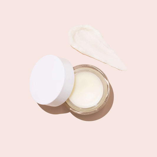 Open jar of creamy multipurpose balm with a dollop on a soft pink background.